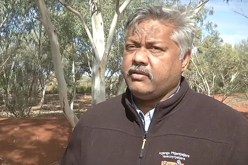 An Indigenous man standing outside in front of a tree.