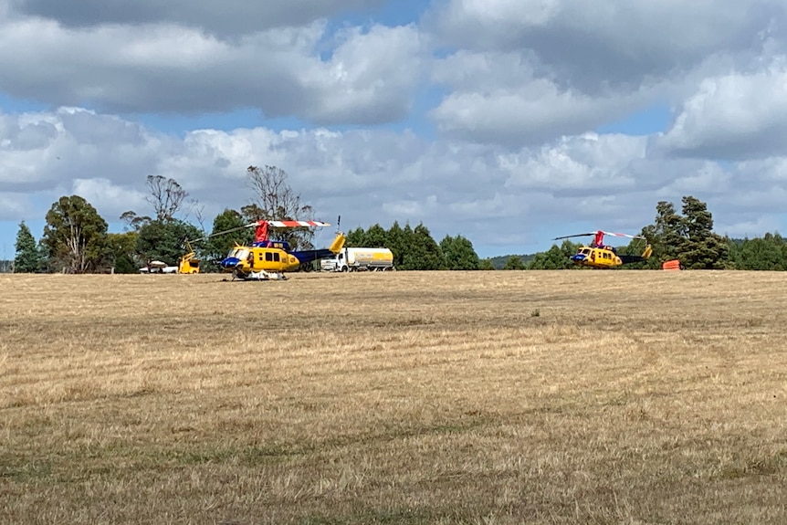 Two helicopters and a petrol tanker in a field. 