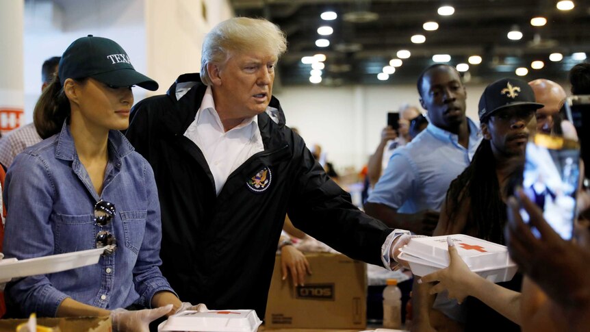 Donald Trump hands a box of food to someone at a relief centre, with his wife Melania by his side
