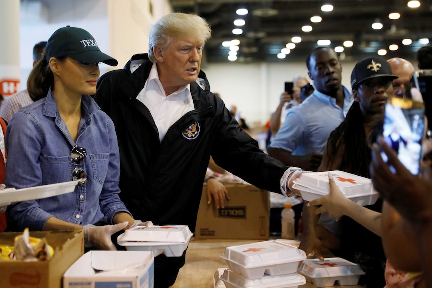 Donald Trump hands a box of food to someone at a relief centre, with his wife Melania by his side