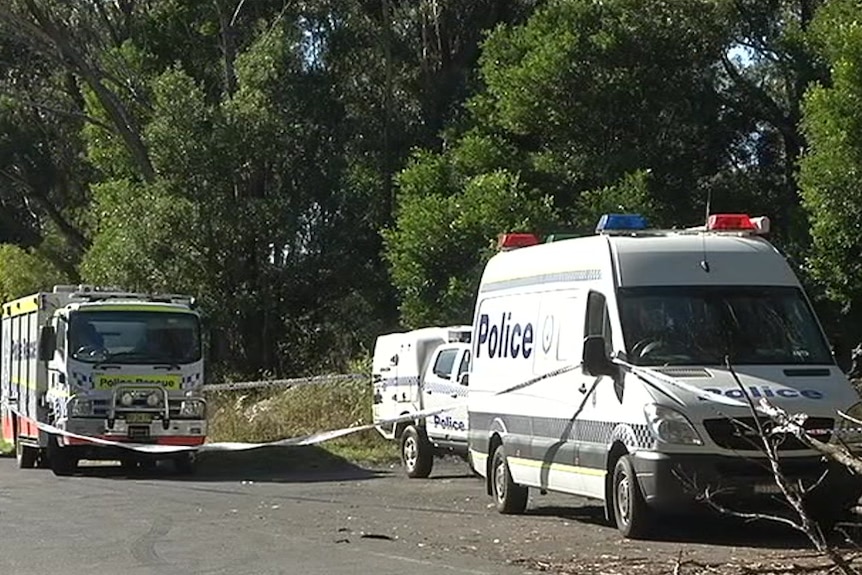 Police tape runs between three police cars parked on the side of the road