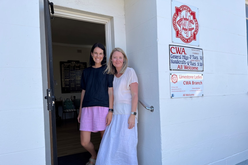 Two women standing in the doorway of a white building with a CWA sign on it