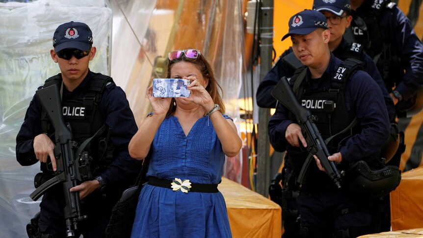 A woman takes photos next to policemen standing guard outside St Regis hotel, in Singapore.