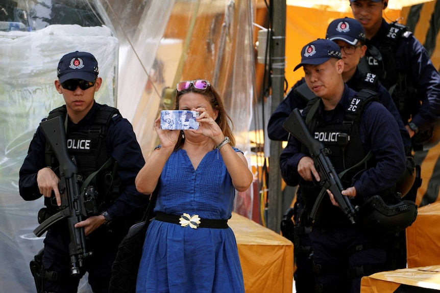 A woman takes photos next to policemen standing guard outside St Regis hotel, in Singapore.