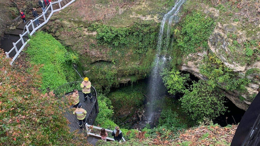 Five people stand on a viewing platform above a sinkhole