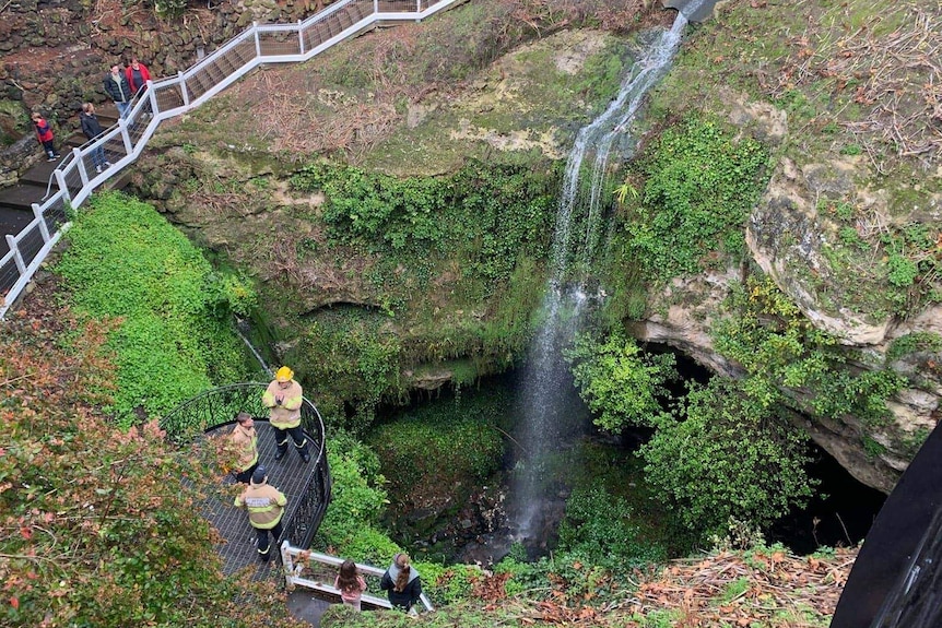Five people stand on a viewing platform above a sinkhole