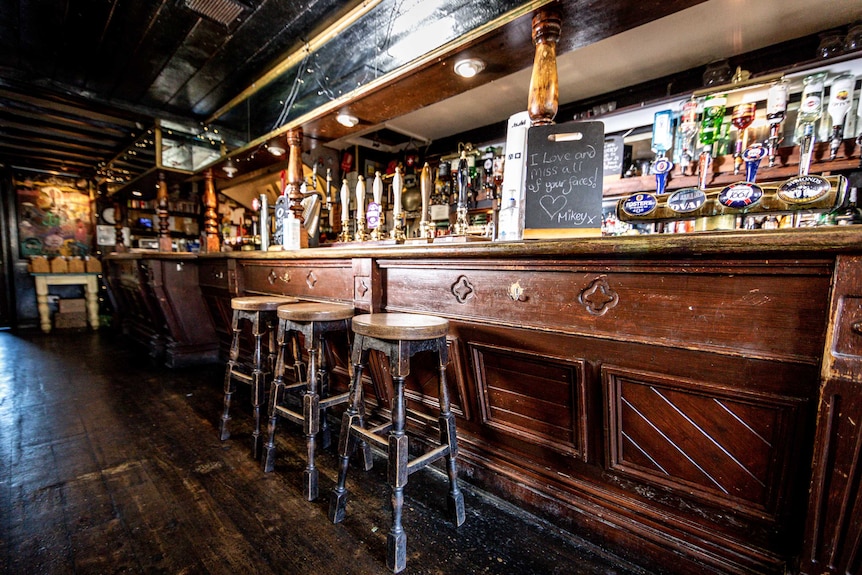 An empty British pub with a sign reading "I love and miss all your faces!"