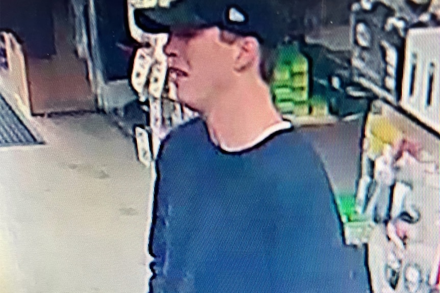 A grainy photo from CCTV footage of a man, wearing a blue long-sleeved T-shirt and a black cap, holding a handgun.