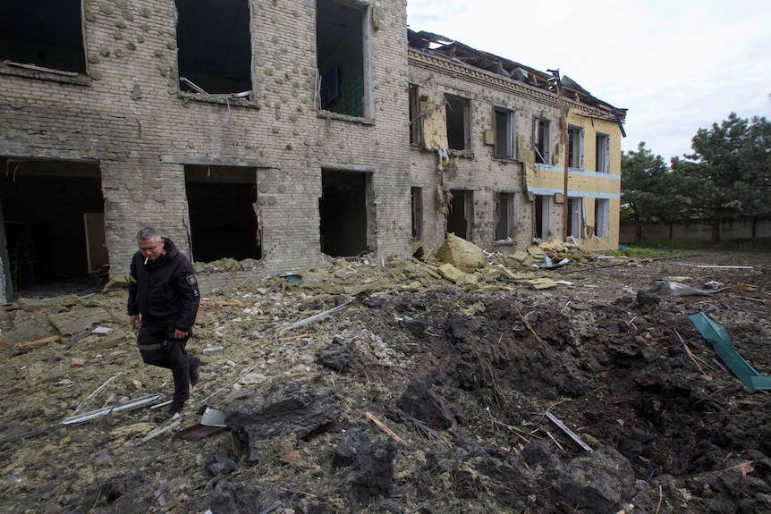 A man with a cigarette in his mouth walks through the rubble of a bombed out building