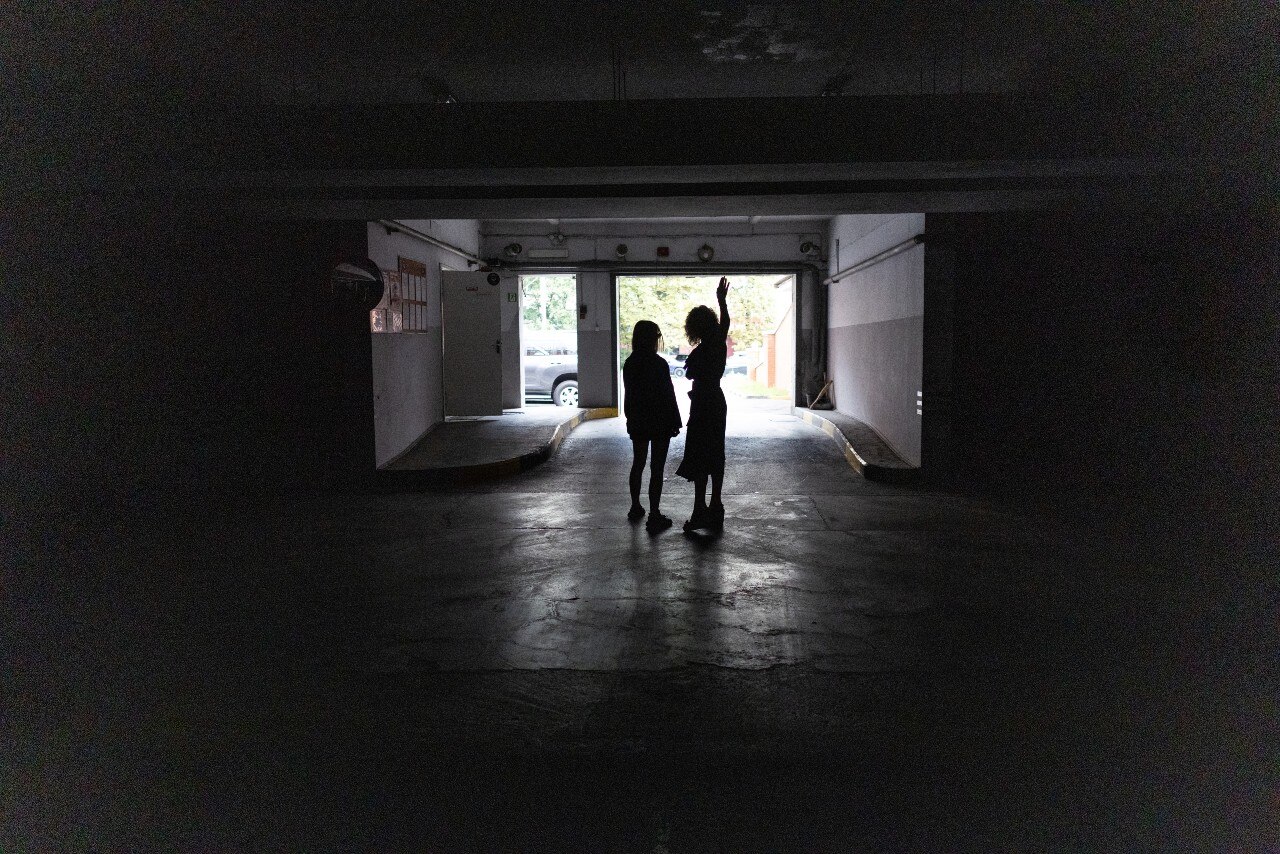 The silhouette of two women standing near the entrance to a car park.