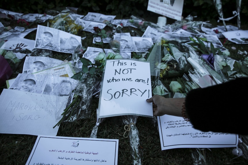 flowers and a sign saying this is not who we are! Sorry! along with photos on the ground