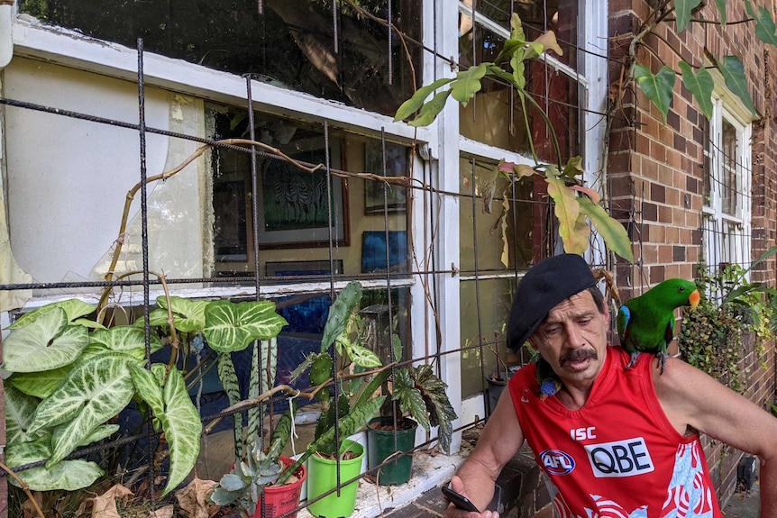 Peter "Pierre" Gawronski leans against the window of his social housing flat, wearing a swans jersey, holding a green parrot.