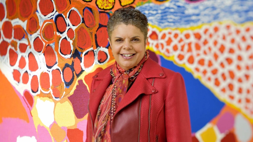 Image of Singer Deborah Cheetham standing in front of Indigenous artwork