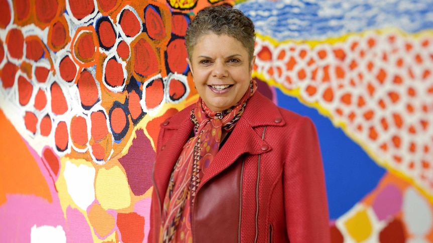Image of Singer Deborah Cheetham standing in front of Indigenous artwork