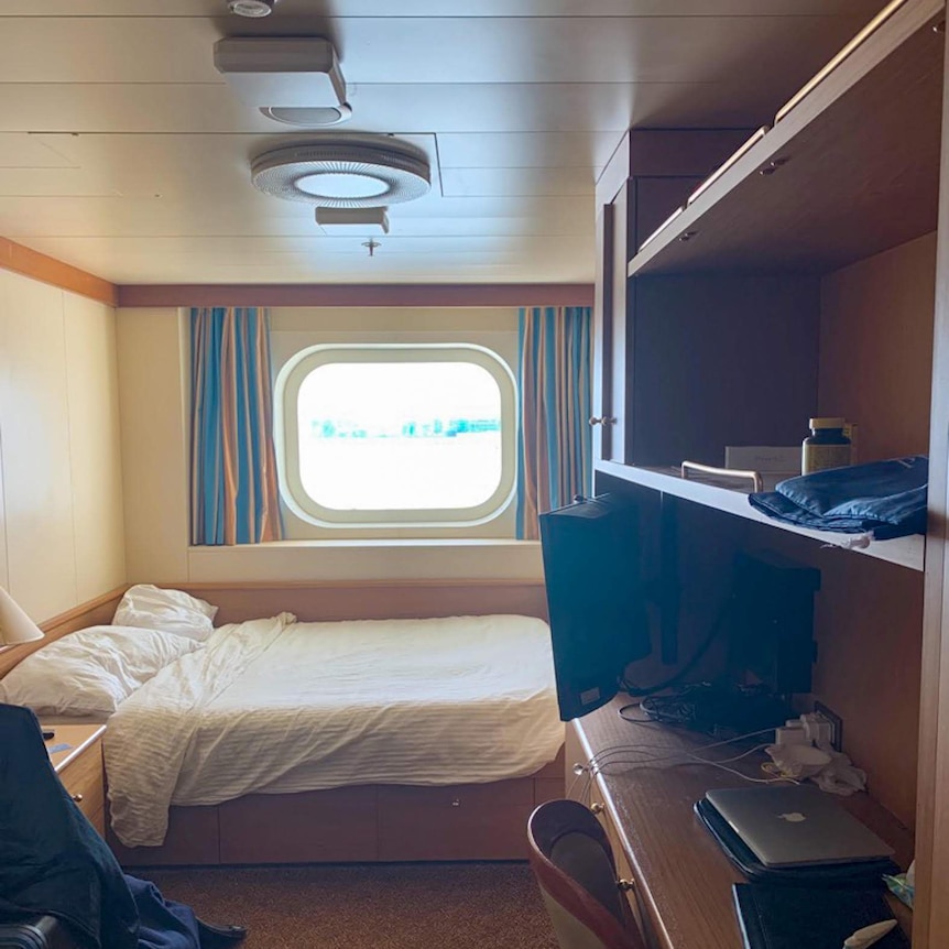 A cabin on a cruise ship, there is a small window and curtains with a bed visable.