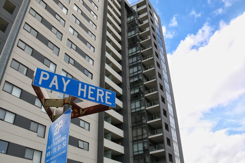 A tall apartment building with a pay parking sign in front of it.