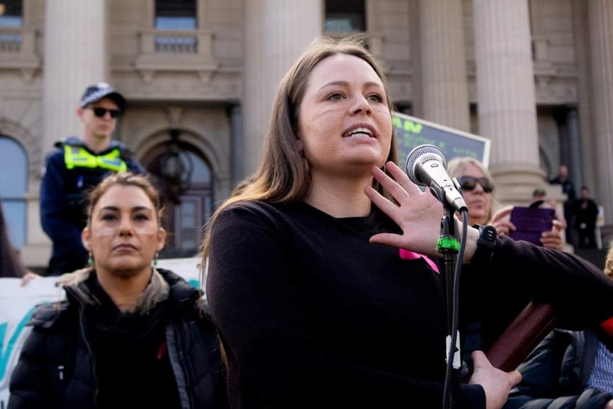 A woman speaks into a microphone in front of the parliament building