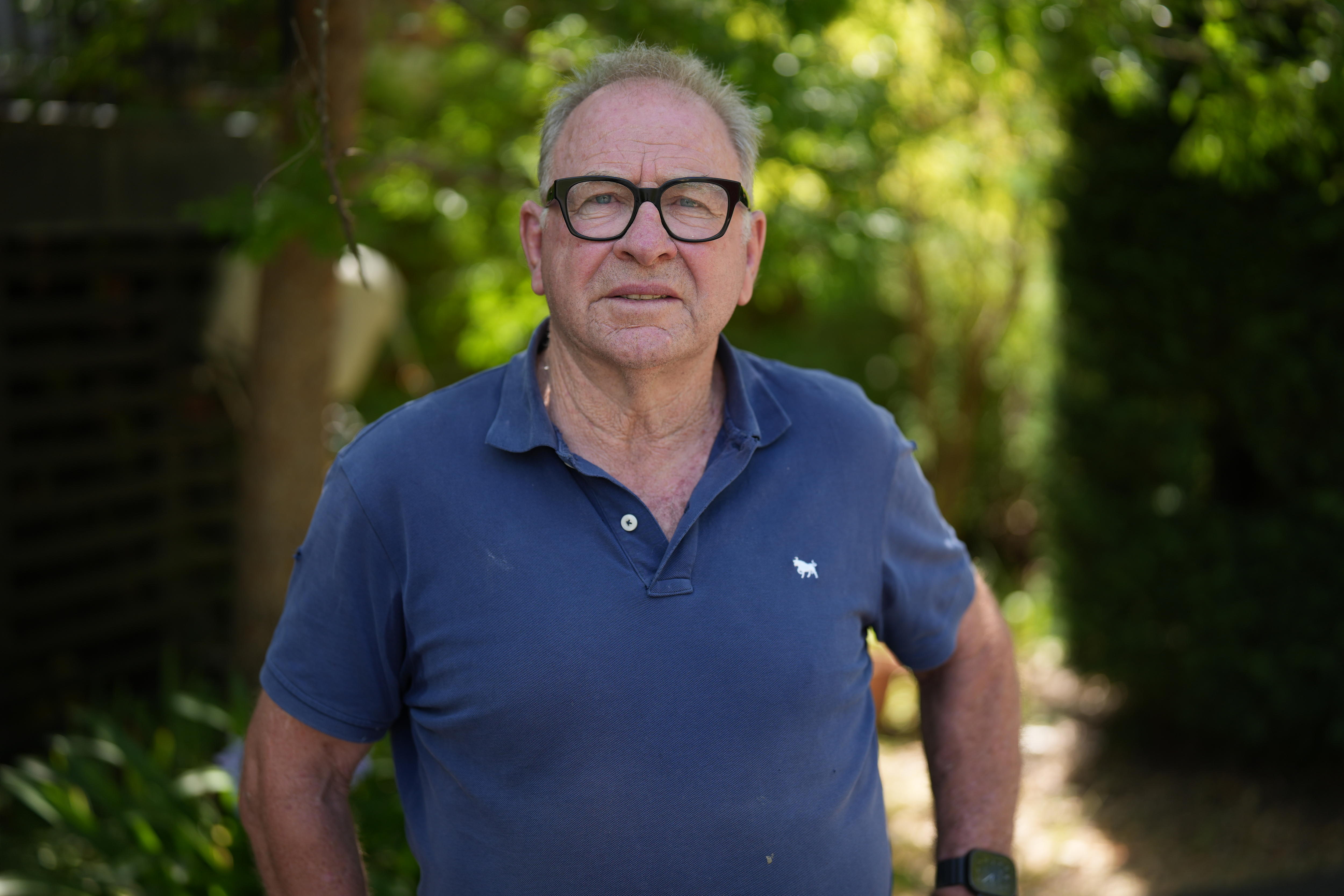Un hombre con gafas negras de montura gruesa, una camiseta azul y pelo corto gris mira a la cámara.