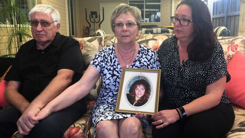 Lisa Govan's father Ian Govan, mother Pat Govan and sister Ginette Jackson sit on a couch holding hands with a framed picture.