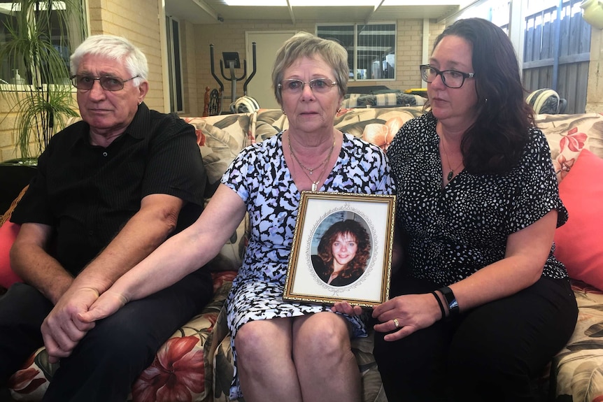 Lisa Govan's father Ian Govan, mother Pat Govan and sister Ginette Jackson sit on a couch holding hands with a framed picture.