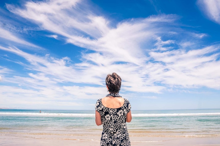 A woman stands looking out over a beach with her back to the camera.