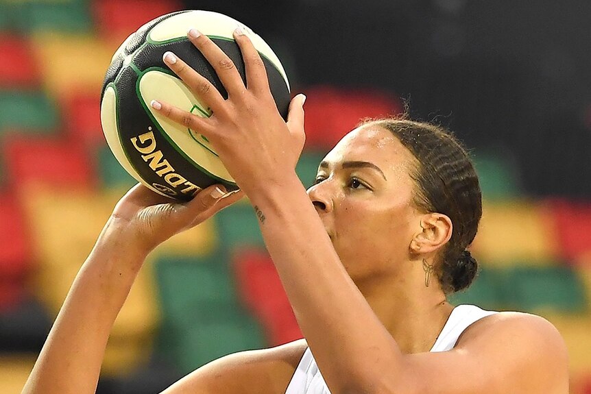 A woman holds a basketball in front of her face, ready to shoot for a basket.