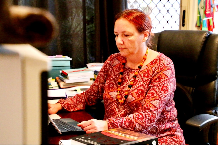 A woman wearing a red dress sits at a desk in front of a computer.