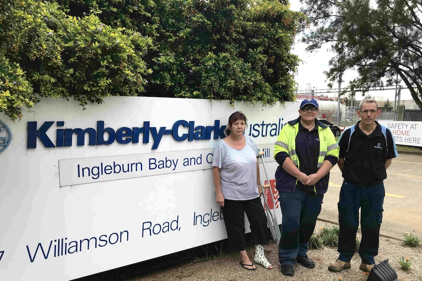 Three people stand in front of a sign which reads Kimberley-Clark.