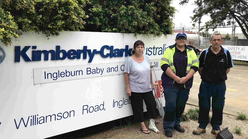 Three people stand in front of a sign which reads Kimberley-Clark.