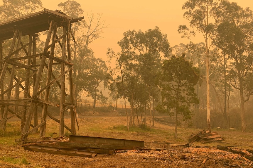 The charred remains of a burnt-out trestle bridge through yellow smoke.