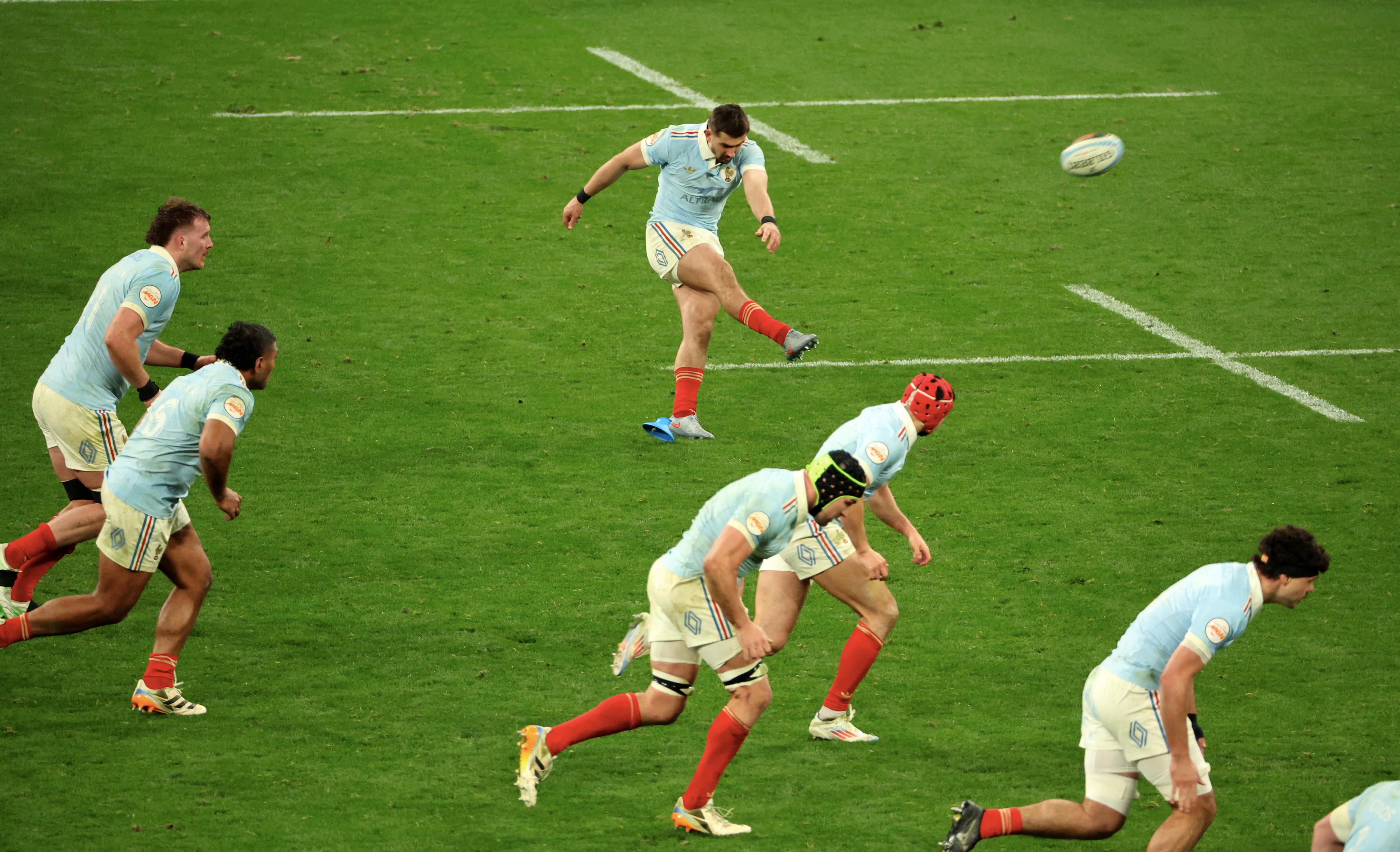 A French rugby union international kicks a ball towards the posts, as his teammates run forward.