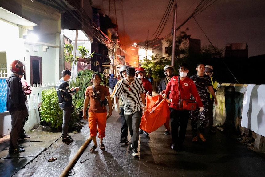 Bystanders look on as rescuers carry a body bag through a street