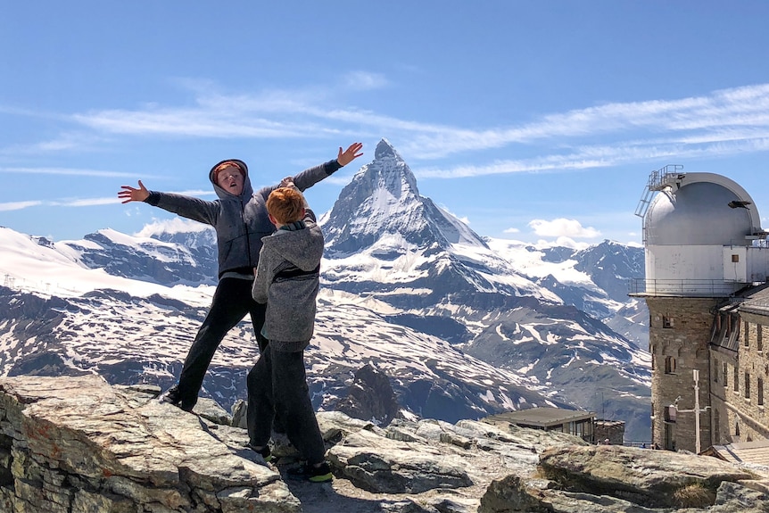 A boy pretends to lose balance as his brother pushes him off what looks like a ledge at a lookout in front of the Matterhorn.