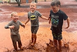 Three smiling kids jump in muddy puddles.