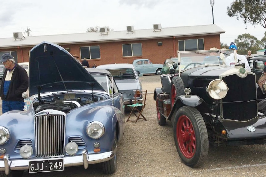 People inspect two vintage cars.