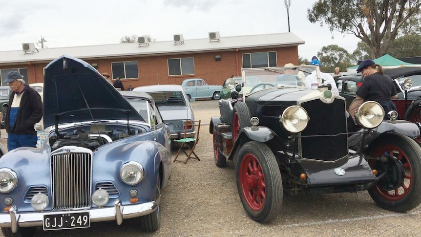 People inspect two vintage cars.