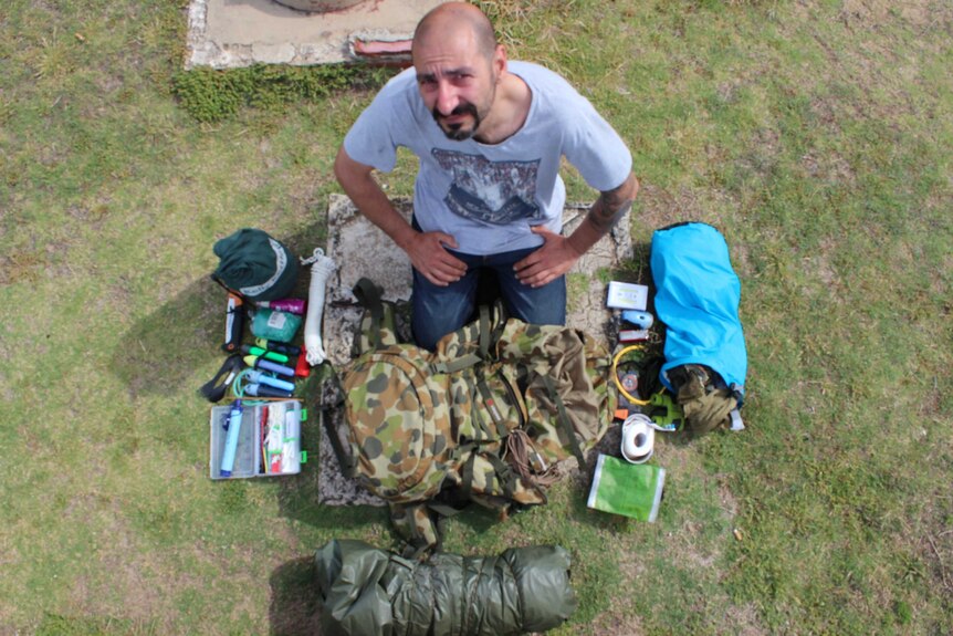 Nick Sais sitting with a bag of survival supplies scattered around him.