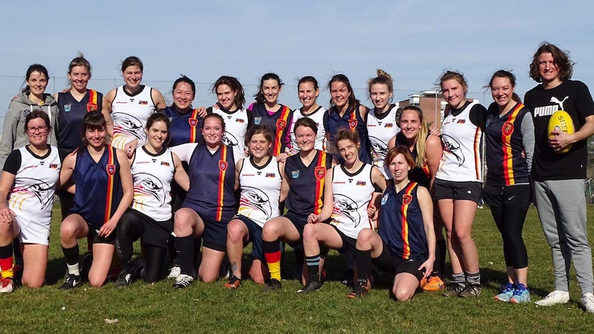 A team of women AFL players pose for a photo on an oval.