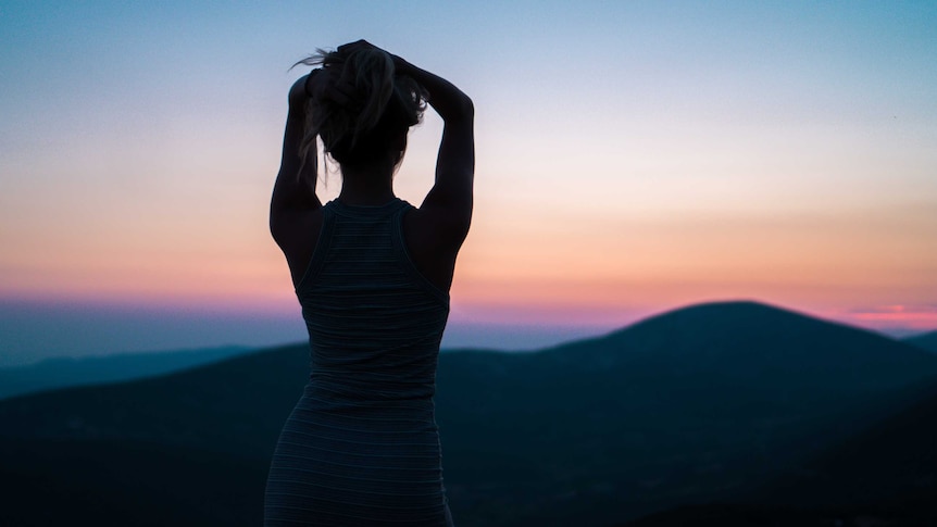 Shadow of woman with arms above head looks into the sunrise for story on women choosing to be childfree