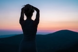 Shadow of woman with arms above head looks into the sunrise for story on women choosing to be childfree