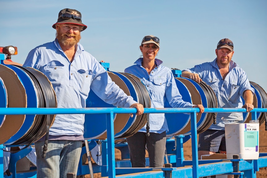 three people in blue shirts standing near machinery