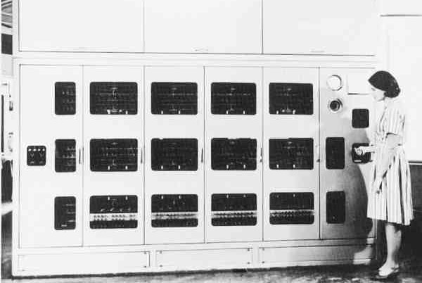 Black and white photo showing a woman standing in front of a computer the size of a shipping container