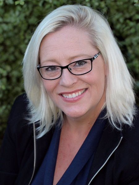 A blonde woman in a suit jacket smiles at the camera