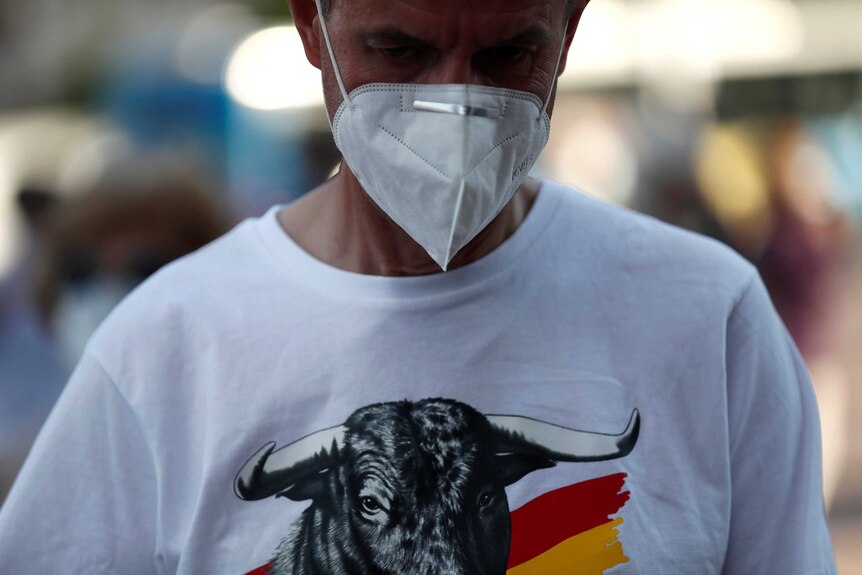 A close up of a man wearing a medical mask and a t-shirt with the Spanish colours and a bull on it.