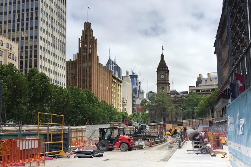 A construction site with machinery, concrete mixer and low-height scaffolding. City in background.