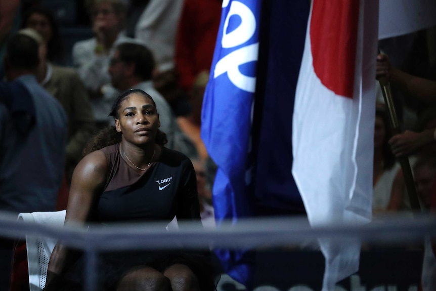 Serena Williams sits on the court next to flags after losing the 2018 US Open final.