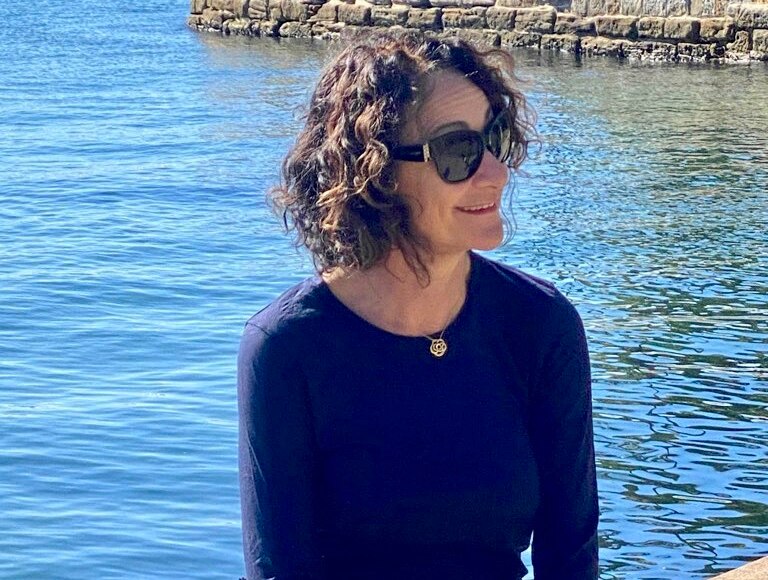 晴れた日に水辺の前で微笑む紺色のトップスの女性。