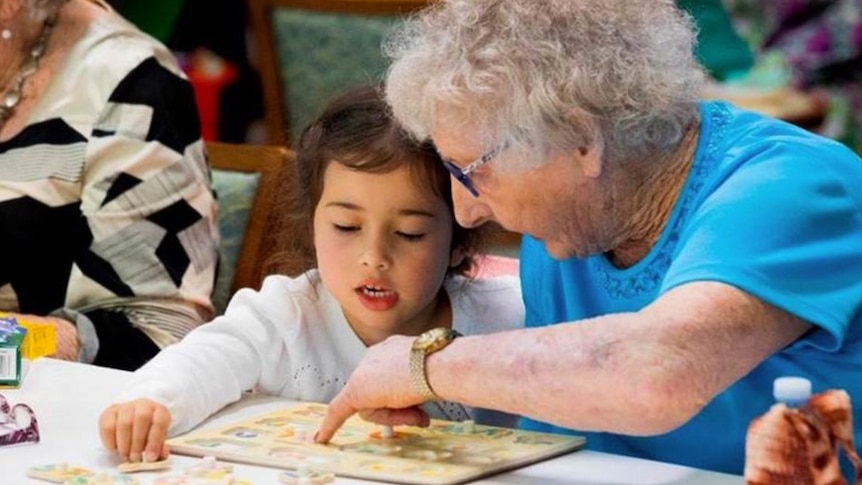 An elderly woman and young girl do a puzzle together