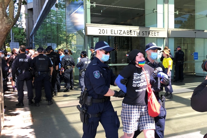 Police arrest a person wearing a rainbow face mask.
