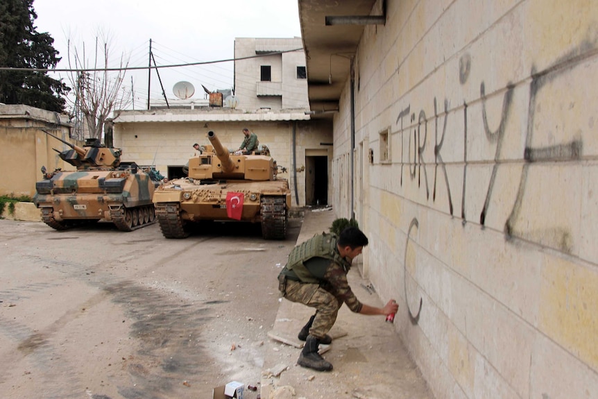 A Turkish soldier writes "Turkey" on a wall, near to tanks in position